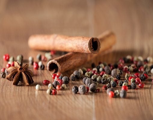 Assorted spices including cinnamon sticks, star anise, and a colorful mix of whole peppercorns scattered across a wooden surface.